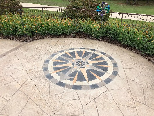 a compass done with a stencil in shades of gray concrete on a tan stamped concrete patio 